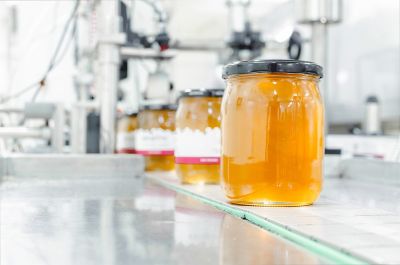 Food and beverage industry: Glass of jam or honey on manufacturing belt about to be processed in a labelling machine